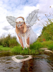 A girl is dressed up as a fairy all in white. She kneels by a river where a white heart is floating...