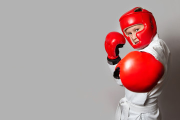 A teenager in a white kimono and gloves and a helmet for hand-to-hand combat on a gray background. Copy space. Sports exercises. Rack of protection.