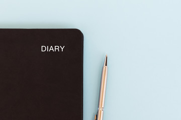 Black diary and pen on blue background with copy space.