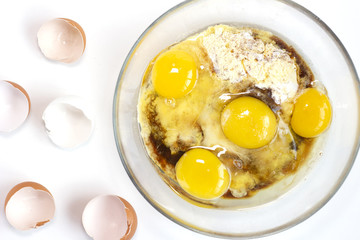Corn and rice flour, coconut sugar, four eggs in the transparent plate. Making a cake. Mixing the dough. White background. Copy space. Place for text and design. Top view. Flat lay. Gluten-free recipe