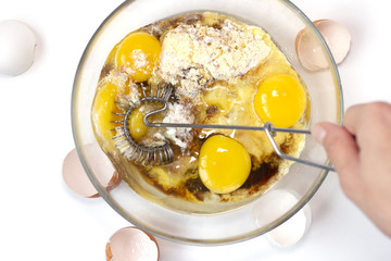 Corn and rice flour, coconut sugar, four eggs in the transparent plate. Making a cake. Mixing the dough. White background. Copy space. Place for text and design. Top view. Flat lay. Gluten-free recipe