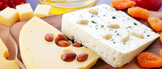 Cheese platter: variety of cheeses on wooden plate with fruits and nuts. Different types of cheese and honey. Hard cheese and berries on a classic blue background. Top view