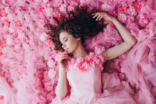 Closeup portrait of a pretty girl in a pink dress. Young woman with curly hair lies on a pink, floral background, top view. The emotional porter of a woman.