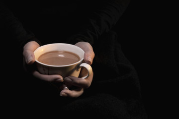 Cup with coffee with milk in the hands of a girl on a black background