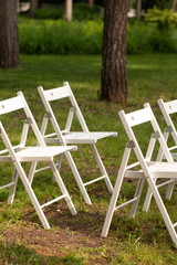 A beautiful place for a wedding ceremony in a clearing in the forest. Many white wooden chairs standing in a row. Luxury wedding ceremony in the open air.