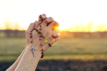 Woman praying outdoor with rosary beads at sunset .