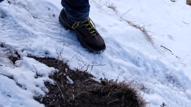 Hiking shoes with yellow laces walking in the snowy ground. Tracking shot, high angle