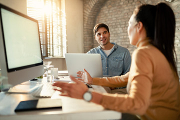Young entrepreneur talking to colleague while working on laptop in the office.
