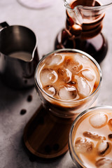 Iced coffee in a glass with ice cubes on wooden tray and concrete background, top view