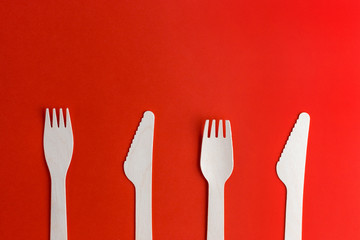Wooden disposable forks, knifes on red background, recycling and eco friendly concept. Zero waste, plastic free items, stop plastic. Top view. Place for text
