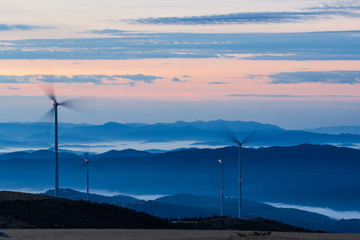 Fototapeta na wymiar Wind turbines on the mountain morning fog at sunset