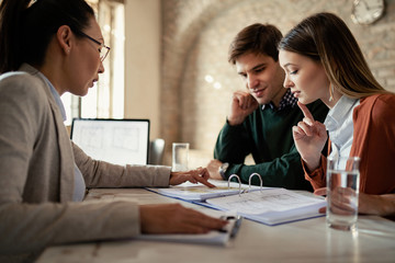 Young couple analyzing paperwork with their insurance agent in the office.