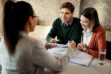 Happy couple talking about terms of a contract with their insurance agent in the office.