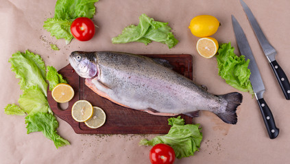 Raw fresh unprepared salmon fish on a wooden board with ingredients for cooking. Lemon, lettuce, tomatoes. Mediterranean cuisine, top view.