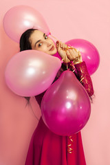 Young pretty woman in red evening dress holding festive air balloons. Portrait of happy 20s middle-eastern female celebrating valentines day, birthday, party