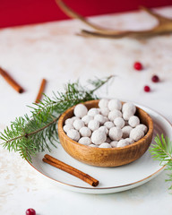 Cranberries in powdered sugar in a wooden plate with a tube of cinnamon and a fir branch. In the background, fresh cranberries and deer horn.