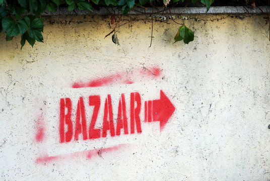 BAZAAR inscription drawn in red paint on a white concrete wall with a red pointing arrow. The inscription indicates the location of the local market. An unforgettable summer vacation in Turkey.