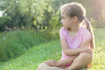 Beautiful little girl in pink t-shirt on grass. Tired girl after walk in the city park