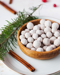 Cranberries in powdered sugar in a wooden plate with a tube of cinnamon and a spruce branch close-up.
