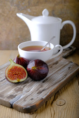 Ripe juicy figs on the cutting board, a cup of tea and a kettle on the table.