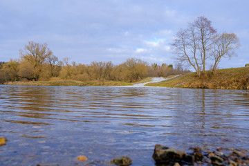 Landscape. Trees, dry grass and a country road along the banks of a small river in late autumn.