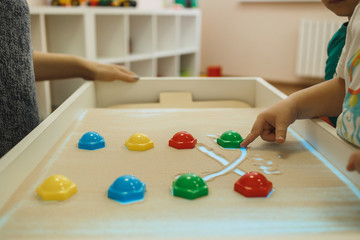 A child plays educational games on an interactive sandy table.