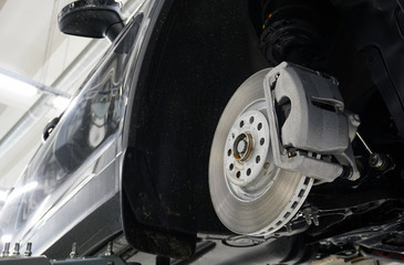 The front brake disc and brake caliper are mounted on a modern car. Design and elements. Original spare parts and quality service and repair.