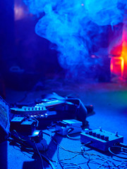 Guitar and guitar equipment lie on stage in fog and smoke in purple, blue and orange lighting.