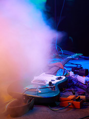 Guitar and guitar equipment lie on stage in fog and smoke in purple, blue and orange lighting.