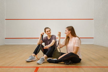 Two players with squash rackets sits on floor