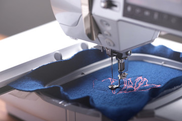 oblique view on machine head and embroidery hoop of a modern sewing machine that stitches a magnolia with light pink yarn on classic blue boiled wool - background and foreground blurry