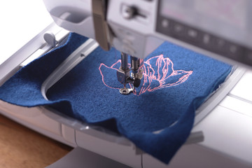 Sewing machine with embroidery unit stitches a light pink magnolia on boiled wool in trendy classic...