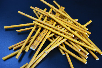 Tasty and sweet straws with poppy seeds made of flour, sneking scattered on a black plastic background.