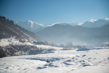 Sunny afternoon deep in the mountains with snowy peaks in the background and a wide snow field with deep snow in the foreground and some footprints in the snow leading into the background.