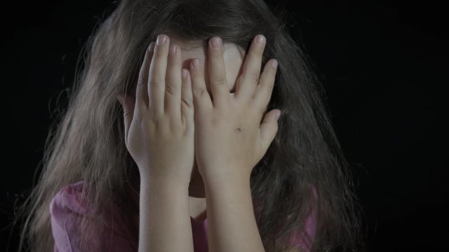 Horror on child face. The little girl hides her face with her palms in fear.