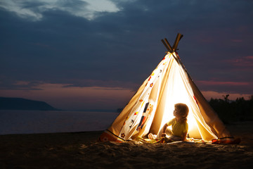 happy child  play in a tent in the evening  on the beach. Summer camp.