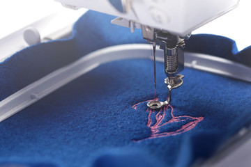 Detail view on a piece of boiled wool fabric in vivid trendy classic blue color that is being equipped with a magnolia embroidery in light pink - background and foreground blurry