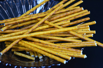 Tasty and sweet straws with poppy seeds made of flour, sneking are located in a brown glass plate on a black plastic background.