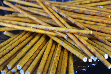 Sweet and salted straws with poppy seeds and salt made from flour, sneking are located in a brown glass plate on a black plastic background.