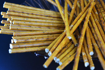 Sweet and salted straws with poppy seeds and salt made from flour, sneking are located in a brown glass plate on a black plastic background.