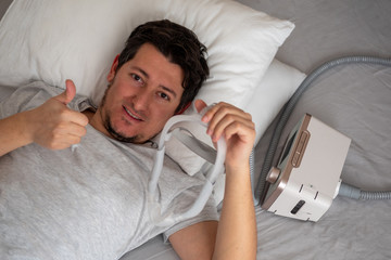 Healthy young man wearing under the nose nasal mask and using CPAP machine for sleeping smoothly...