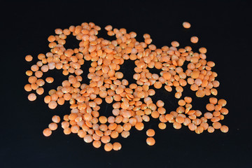 Grains, seeds of red lentils, a handful of lentils are located and scattered on a black plastic background.