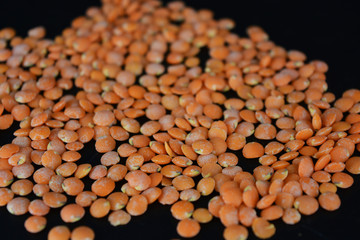 Grains, seeds of red lentils, a handful of lentils are located and scattered on a black plastic background.