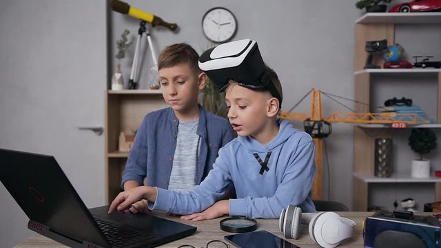 Attractive serious 7-10 aged boy choosing the video game on computer to play with his friend using virtual reality headset