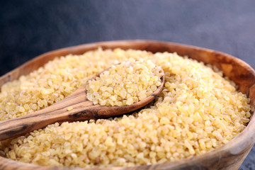 Uncooked bulgur in wooden spoon, rustic style. Healthy Bulgur wheat grains