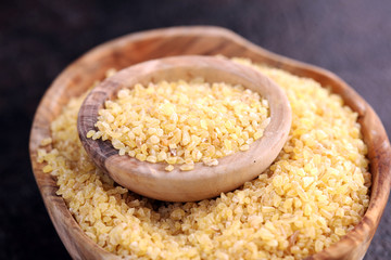 Uncooked bulgur in wooden spoon, rustic style. Healthy Bulgur wheat grains