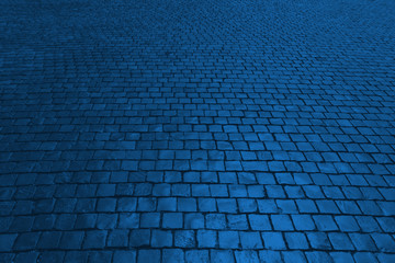 Old cobblestone pavement in perspective in color Pantone classic blue 2020. Color of the year. Abstract background. Monochrome photo.