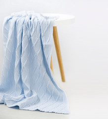 Blue knitted plaid falls from the stool. White background. Handmade.