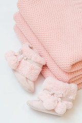 Folded knitted pink plaids. Next to them are fluffy pink baby boots.
