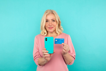 Fototapeta premium Happy woman in the pink dress holding credit card with mobile